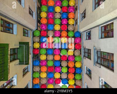 Affichage suspendu vibrant de parapluies multicolores suspendus entre deux bâtiments dans une cour urbaine étroite à Łódź, Pologne Banque D'Images