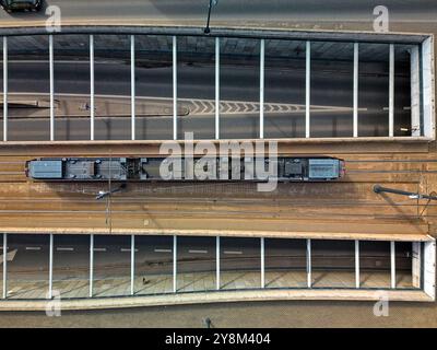 Vue aérienne d'un tramway unique voyageant sur un pont au-dessus d'une route à Łódź, Pologne, capturée directement au-dessus, avec des motifs symétriques de rails et R. Banque D'Images