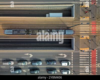 Vue aérienne d'un tramway unique voyageant sur un pont au-dessus d'une route à Łódź, Pologne, capturée directement au-dessus, avec des motifs symétriques de rails et R. Banque D'Images