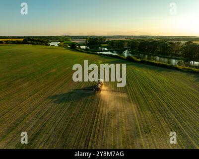 Photo drone d'un tracteur pulvérisant dans des champs de blé verdoyants sous le soleil brillant, mettant en valeur l'agriculture moderne Banque D'Images