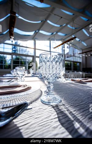 Verre de cristal sur la table dans une salle de banquet lumineuse aux parois de verre. Photo prise pendant la journée, avec la lumière du soleil. Banque D'Images