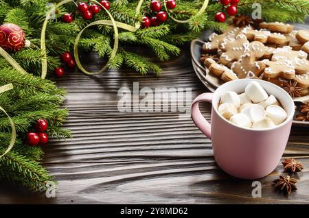 Noël arrière-plan de mug rose avec du chocolat chaud et des guimauves, de la direction générale de l'épinette et du bac avec gingerbread man cookies sur table en bois Banque D'Images