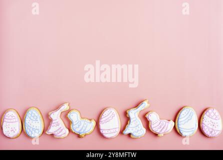 Biscuits givrés de Pâques en forme d'oeuf, de lapin et de poulet sur fond rose. Pose à plat avec espace de copie Banque D'Images