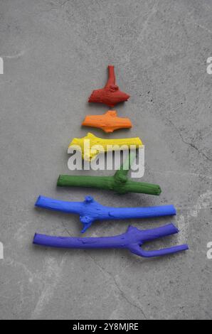 Mise à plat de l'arbre de Noël stylisée faite de petites brindilles peint en couleurs arc-en-ciel sur fond de pierre. Un espace réservé au texte Banque D'Images