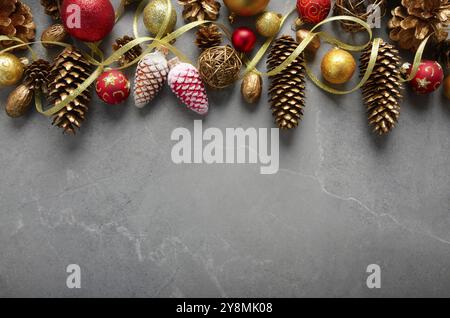 Vue plate sur les décorations de Noël de billes de verre rouge et jaune de cônes dorés et ruban sur la table en pierre. Espace pour le texte Banque D'Images