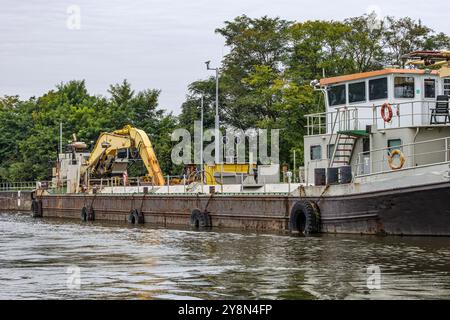 Ancien navire industriel avec une excavatrice sur le pont, ancré au petit quai sur la rive de la Meuse, arbres verdoyants sur fond gris ciel, clou Banque D'Images