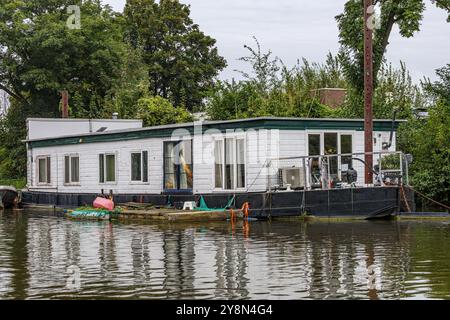 Péniche avec murs blancs et toit plat ancré sur la rive du canal maritime en dehors de la ville de Maastricht, avec des arbres verts en arrière-plan, jour nuageux Banque D'Images