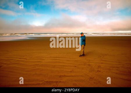 Un homme d'affaires senior célibataire utilise un téléphone cellulaire pour faire des affaires sur une plage vide de la péninsule olympique. Etat de Washington. Banque D'Images