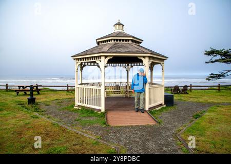 Un homme d'affaires senior célibataire utilise un téléphone cellulaire pour passer un appel sous l'abri d'un belvédère au Kalaloch Lodge. Etat de Washington. Banque D'Images