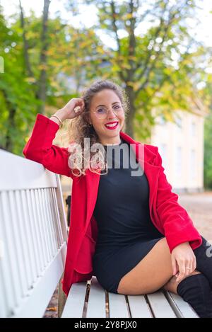 fröhliche Junge Frau mit brille sitzt auf einer Bank im Park *** jeune femme joyeuse avec des lunettes est assise sur un banc dans le parc Banque D'Images