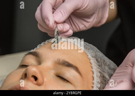 Le concept de cosmétologie. Gros plan d'une esthéticienne appliquant un masque vert avec un pinceau sur le visage d'une femme. Banque D'Images