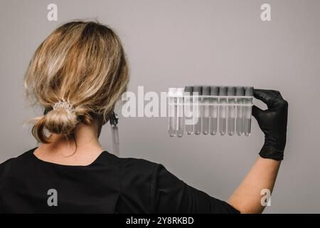 Vider le tube à essai dans une fiole en verre dans les mains d'un scientifique ou d'un cosmétologue. Gants noirs sur fond gris. Expérience, analyses, fille de la Banque D'Images