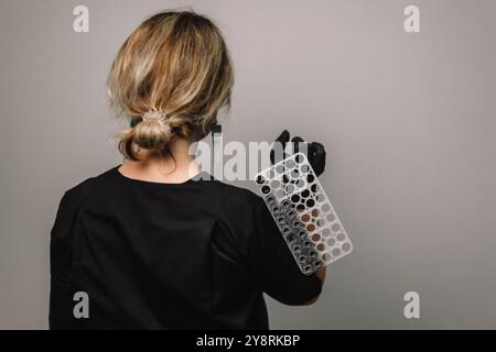 Vider le tube à essai dans une fiole en verre dans les mains d'un scientifique ou d'un cosmétologue. Gants noirs sur fond gris. Expérience, analyses, fille de la Banque D'Images