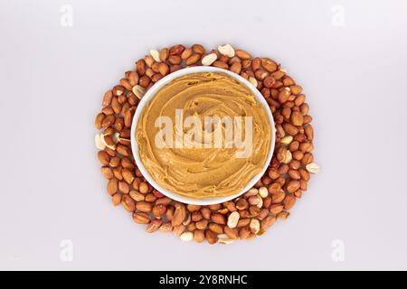 Beurre d'arachide crémeux, beurre d'arachide dans un pot en verre ouvert au centre d'un fond alimentaire d'arachide. Cacahuètes en coquille, cacahuètes pelées sur un blanc Banque D'Images