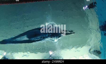 nageuse sportive en survêtement, en lunettes de plongée, en bonnet de natation s'entraîne dans la piscine. L'athlète plonge dans l'eau. Shootine sous-marine Banque D'Images