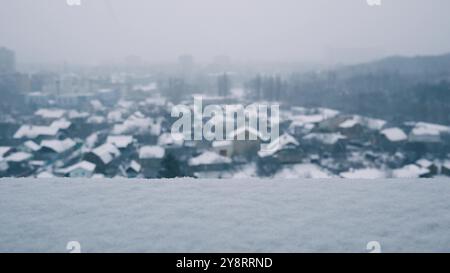 Une couche de neige blanche même gelée repose sur le rebord d'une fenêtre de grande hauteur par temps ensoleillé d'hiver. Les flocons de neige tourbillonnent et tombent sur le groun flou Banque D'Images