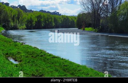 Rivière Hutt, Nouvelle-Zélande, avec un enfant et un adulte debout sur une rive de pierre basse à un virage de la rivière. Croissance printanière luxuriante le long des deux rives Banque D'Images