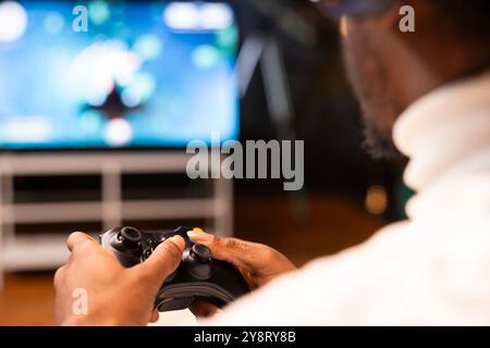 Gros plan des boutons de spamming du joueur sur la manette tout en essayant de terminer un jeu vidéo difficile à la maison. Homme utilisant Gamepad sur la console de jeu pour vaincre les ennemis sur l'écran ultra-large Smart TV Banque D'Images