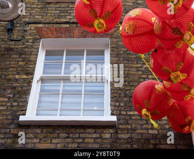 Londres, Royaume-Uni - 25 juin 2024 : une fenêtre à cadre blanc sur un mur de briques avec des lanternes chinoises rouges suspendues à proximité - China Town à Londres Banque D'Images