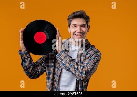 Homme mature élégant avec disque vinyle sur jaune. Hobby, musique, collection Banque D'Images