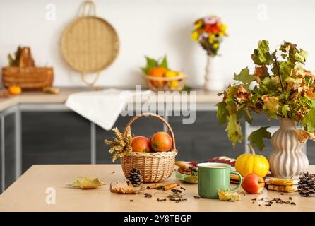 Vase avec des feuilles d'automne, tasse de thé vert chaud, panier avec des pommes et des épices sur la table dans la cuisine Banque D'Images