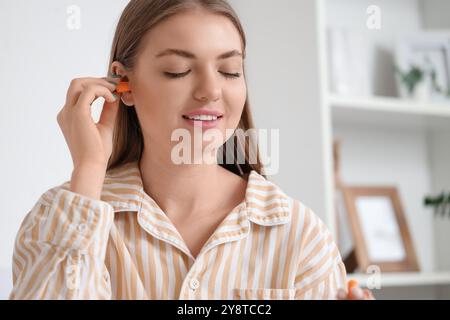 Jeune femme mettant des bouchons d'oreilles dans la chambre, gros plan Banque D'Images