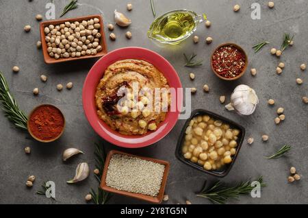 Houmous recouvert de pois chiches, huile d'olive et tomate séchée au soleil sur table en pierre avec différentes épices de côté. Pose plate Banque D'Images