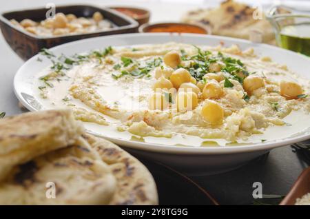 Vue rapprochée sur le Hummus recouvert de haricots d'huile d'olive et de feuilles de coriandre verte sur la table de cuisine avec pain pita Banque D'Images