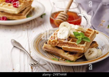 Gaufres belges servies avec banane et feuille de menthe sur blanc table de cuisine en bois avec sirop de côté Banque D'Images