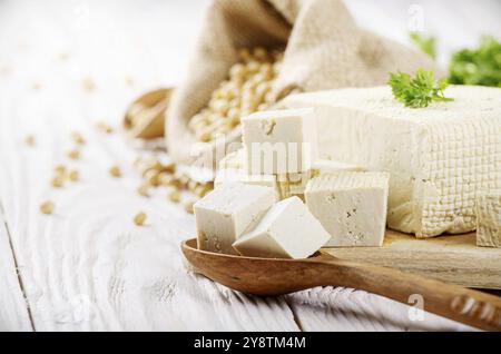 Tofu caillé de soja sur une planche à découper et dans le chanvre sac sur une table de cuisine en bois blanc. Un espace réservé au texte Banque D'Images