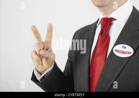 Homme caucasien d'âge moyen en costume avec épingle à bouton je suis vacciné montrant le geste V. Banque D'Images