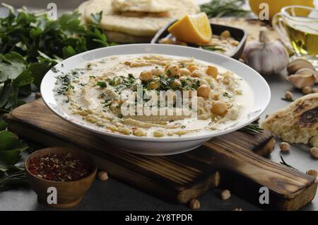 Hummus frais maison dans un plat d'argile recouvert d'huile d'olive, de pois chiches et de feuilles de coriandre verte hachées sur une table en pierre servie avec des épices Banque D'Images