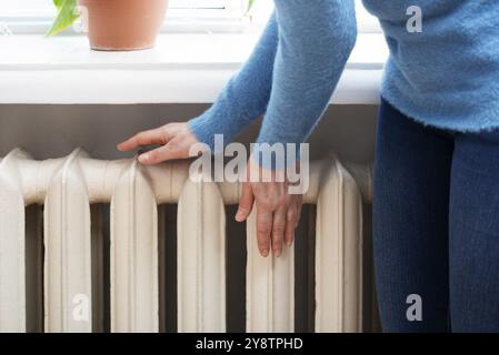 Femme caucasienne réchauffant les mains près du radiateur à eau chaude. Espace pour le texte Banque D'Images