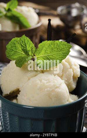 Boules de glace à la vanille dans des bols en argile sur une table de cuisine en bois avec une cuillère à glace de côté Banque D'Images