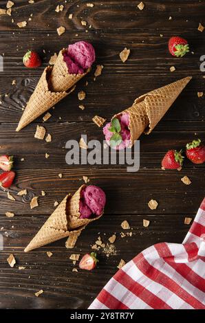 Cônes de cachets avec glace à la fraise sur une table de cuisine en bois avec chapelure et baies de côté Banque D'Images