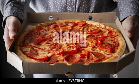 Les mains masculines caucasiennes tiennent une grande boîte en carton ouverte avec vue avant de pizza pepperoni Banque D'Images