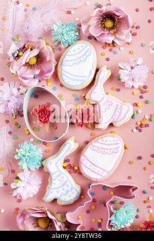 Saupoudrés de sucre, emporte-pièces, biscuits givrés de Pâques en forme d'œuf et de lapin sur fond rose.Maquette de pose à plat Banque D'Images