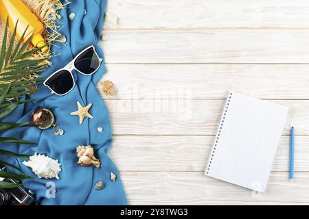 Fond de planification de vacances de coquillages de cahier, étoiles de mer, lunettes de soleil, boussole, appareil photo et chapeau de paille sur tissu bleu et planches blanches à plat avec Banque D'Images