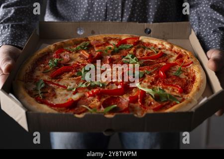 Les mains masculines caucasiennes tiennent une grande boîte de carton ouverte avec pizza pepperoni avec vue de face roquette Banque D'Images