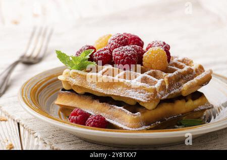 Gaufres belges servies avec framboises et feuilles de menthe sautées sucre en poudre sur une table de cuisine en bois blanc Banque D'Images