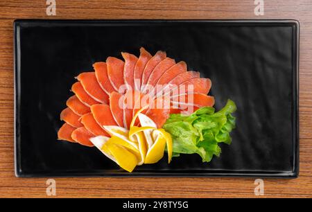 couper l'apéritif de tranches de poisson rouge sur une plaque noire sur une vue de dessus de table en bois Banque D'Images