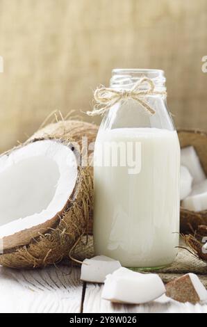 Le flacon en verre de lait ou de yogourt sur le chanvre serviette sur une table en bois blanc à la noix de coco de côté Banque D'Images