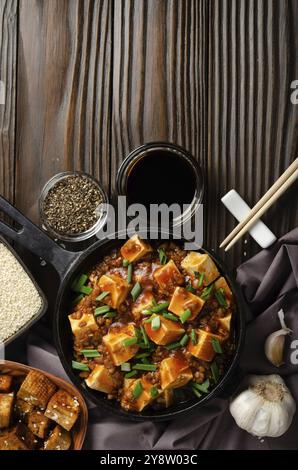 Mapo tofu dans une poêle en fonte avec ciboulette hachée de porc sauce soja poivre du sichuan ail et épices en gros plan sur une table en bois.Pose à plat Banque D'Images