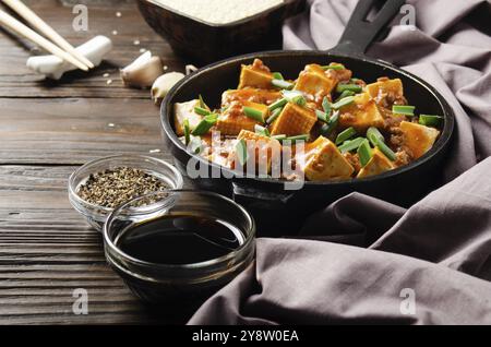 Mapo tofu dans une poêle en fonte avec ciboulette hachée de porc sauce soja poivre du sichuan ail et épices à proximité sur une table en bois Banque D'Images