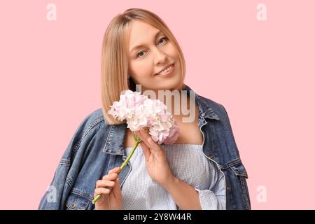 Belle jeune femme avec la coiffure bob tenant des fleurs d'hortensia sur fond rose Banque D'Images