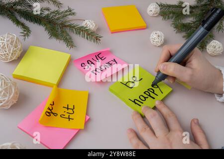 Mains féminines écrivant des résolutions manuscrites du nouvel an vise des objectifs sur des notes autocollantes. Préparation pour le nouvel an. Concept de planification et d'établissement d'objectifs de développement personnel Banque D'Images