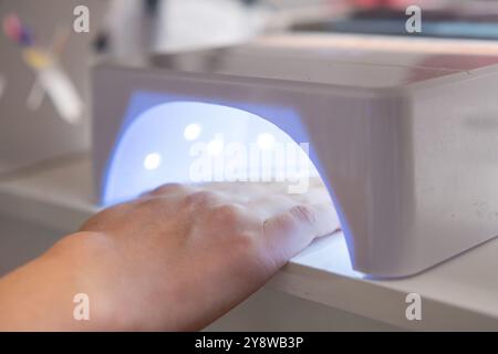 Womans Hand est placé sous une lampe UV pour traiter le vernis à ongles gel après une manucure. Banque D'Images