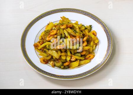 Gourde amère, pommes de terre et crevettes frites mélangées et cuites, servies dans une assiette blanche. C'est un plat de légumes très sain et délicieux. Banque D'Images