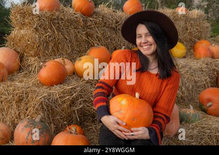 Portrait d'une femme tenant une citrouille assise sur des balles de foin Banque D'Images