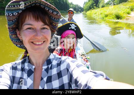 Couple homme et femme, enfant dans un chapeau de pirate, selfies sont heureux en famille kayak voyage bateau à rames sur la rivière, randonnée aquatique, aventure estivale. Écologique a Banque D'Images